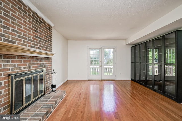 unfurnished living room with wood finished floors, baseboards, a fireplace, and a textured ceiling