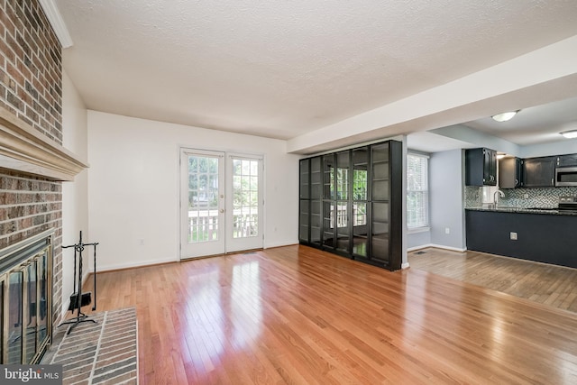 unfurnished living room featuring a brick fireplace, light wood-style flooring, a sink, baseboards, and a textured ceiling