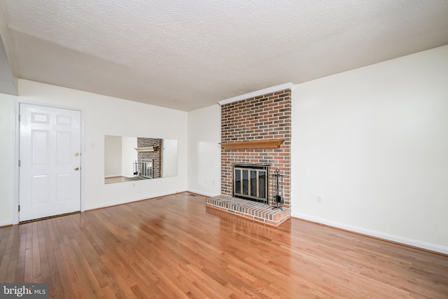 unfurnished living room featuring a brick fireplace, wood finished floors, baseboards, and a textured ceiling