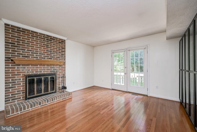 unfurnished living room with wood-type flooring, baseboards, a fireplace, a textured ceiling, and french doors