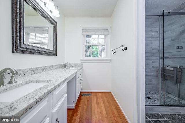 full bath featuring baseboards, a shower stall, double vanity, and wood finished floors
