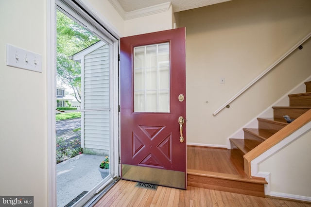 entryway with light wood-style flooring, stairs, healthy amount of natural light, baseboards, and ornamental molding