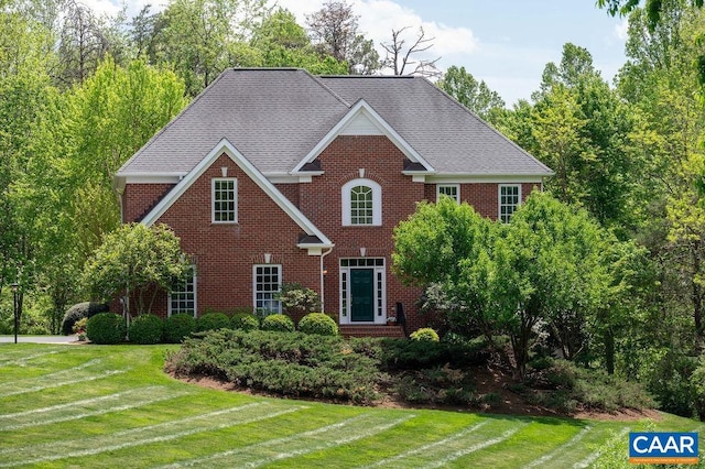 colonial house featuring brick siding, a front lawn, and a shingled roof