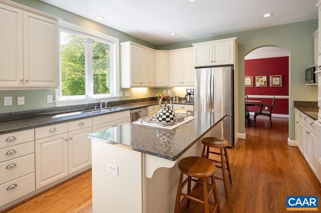 kitchen featuring appliances with stainless steel finishes, a sink, arched walkways, a kitchen bar, and light wood-style flooring