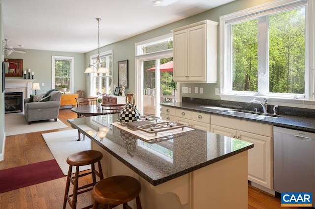kitchen featuring stainless steel dishwasher, a sink, white gas cooktop, a glass covered fireplace, and a breakfast bar area