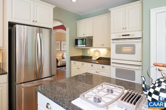 kitchen featuring stainless steel appliances, arched walkways, white cabinetry, dark stone counters, and recessed lighting