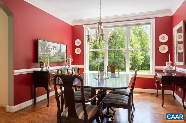 dining room featuring crown molding, arched walkways, wood finished floors, a chandelier, and baseboards