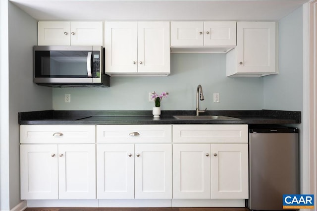 kitchen featuring stainless steel appliances, a sink, white cabinets, and dark countertops