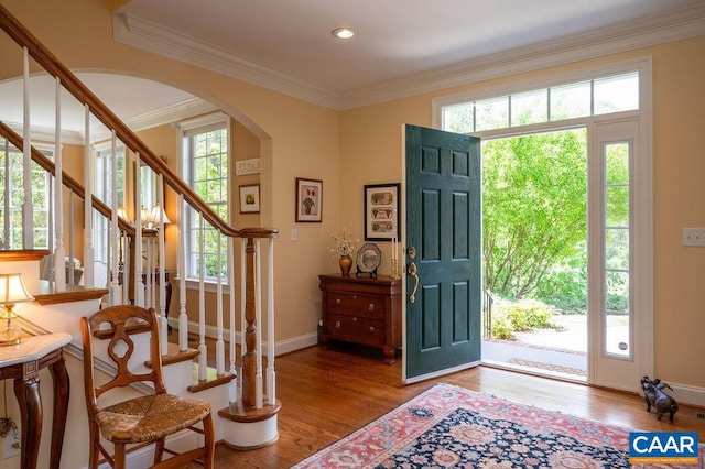 entryway with arched walkways, stairway, wood finished floors, crown molding, and baseboards