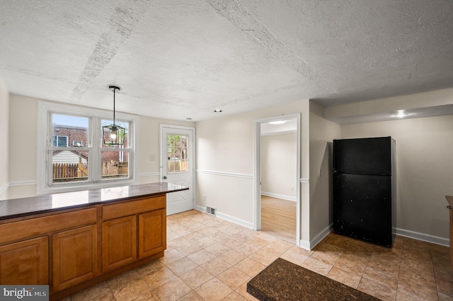 kitchen featuring freestanding refrigerator, dark countertops, visible vents, and brown cabinetry