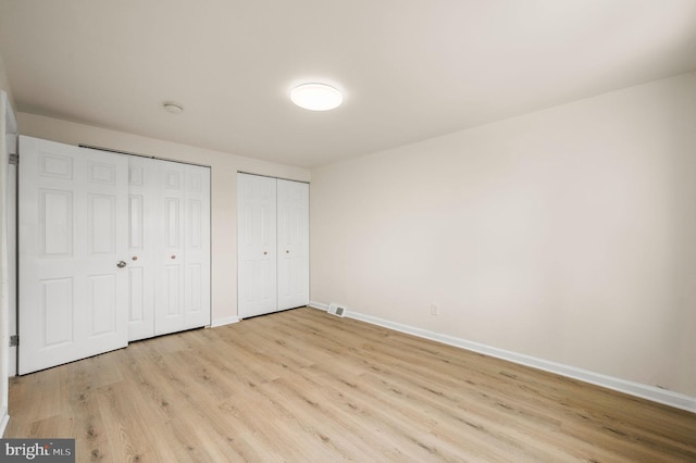 unfurnished bedroom with baseboards, light wood finished floors, visible vents, and two closets