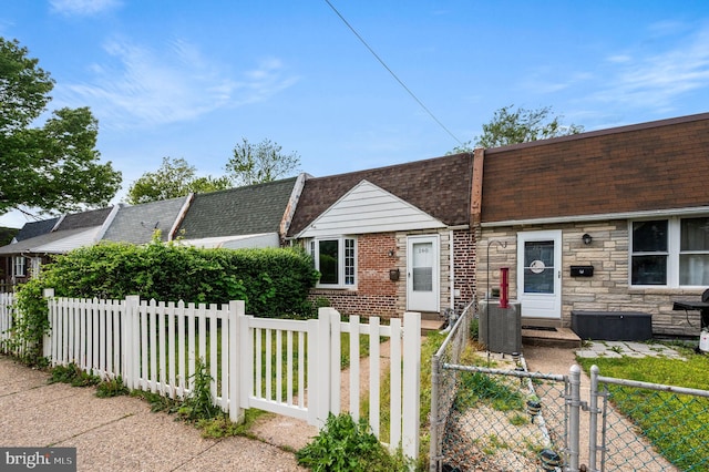 view of front of property featuring stone siding, a gate, central AC, a shingled roof, and a fenced front yard