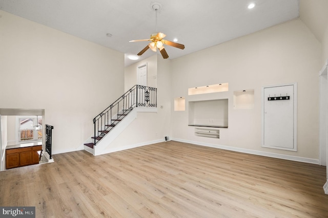 unfurnished living room featuring stairway, ceiling fan, high vaulted ceiling, and wood finished floors