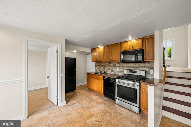 kitchen featuring brown cabinetry, a sink, backsplash, black appliances, and dark countertops