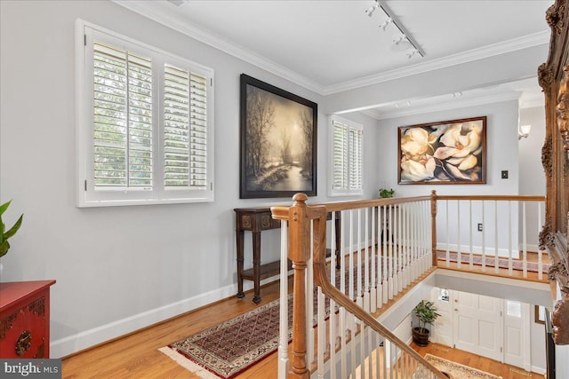 stairway with rail lighting, wood finished floors, plenty of natural light, and ornamental molding