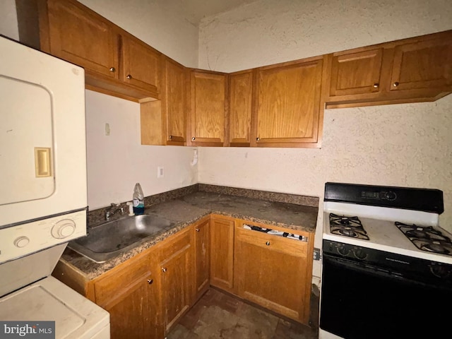kitchen with range with gas stovetop, stacked washing maching and dryer, brown cabinets, and a sink