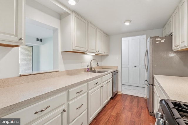 kitchen with dark wood-style flooring, a sink, light countertops, white cabinets, and appliances with stainless steel finishes