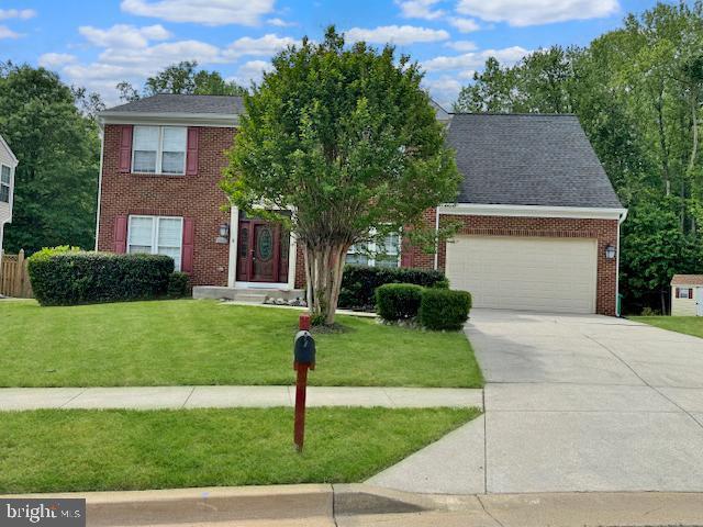 colonial-style house with an attached garage, a front lawn, driveway, and brick siding