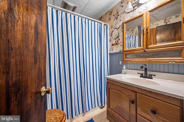 full bath with a shower with curtain, vanity, visible vents, wainscoting, and wallpapered walls