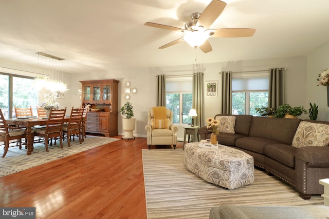 living room featuring light wood-style flooring, ceiling fan with notable chandelier, and a healthy amount of sunlight