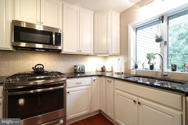 kitchen with a sink, stainless steel appliances, dark stone countertops, white cabinetry, and decorative backsplash