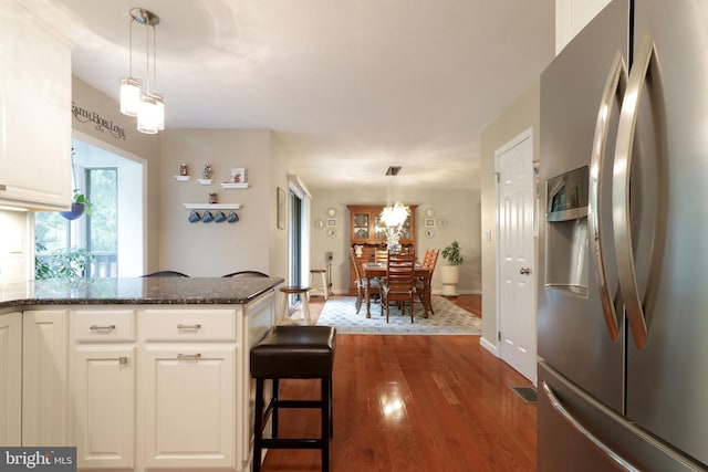kitchen featuring stainless steel fridge, wood finished floors, dark stone countertops, white cabinets, and decorative light fixtures