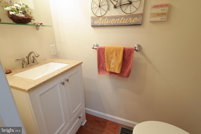 half bath with baseboards, toilet, visible vents, vanity, and wood finished floors