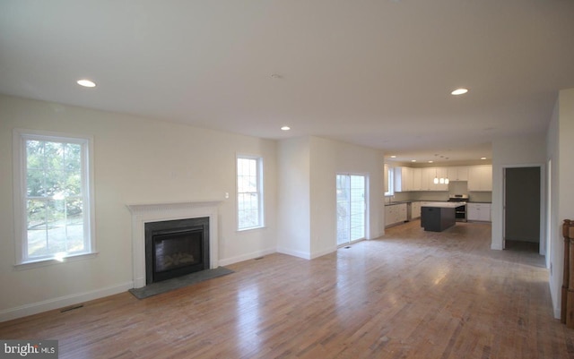 unfurnished living room with plenty of natural light, a glass covered fireplace, recessed lighting, light wood finished floors, and baseboards