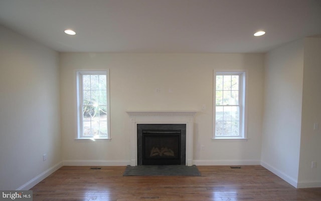 unfurnished living room with wood finished floors, plenty of natural light, a fireplace with raised hearth, recessed lighting, and baseboards