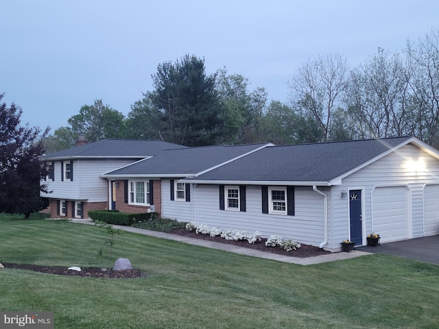 tri-level home with roof with shingles, an attached garage, driveway, a front lawn, and a chimney