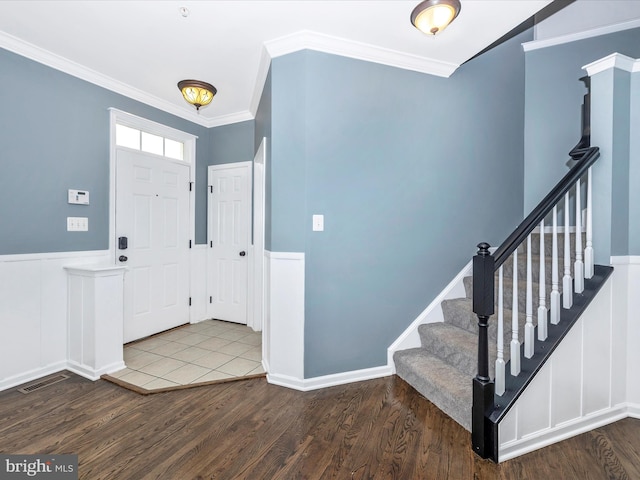 foyer with wood finished floors, ornamental molding, wainscoting, and stairway