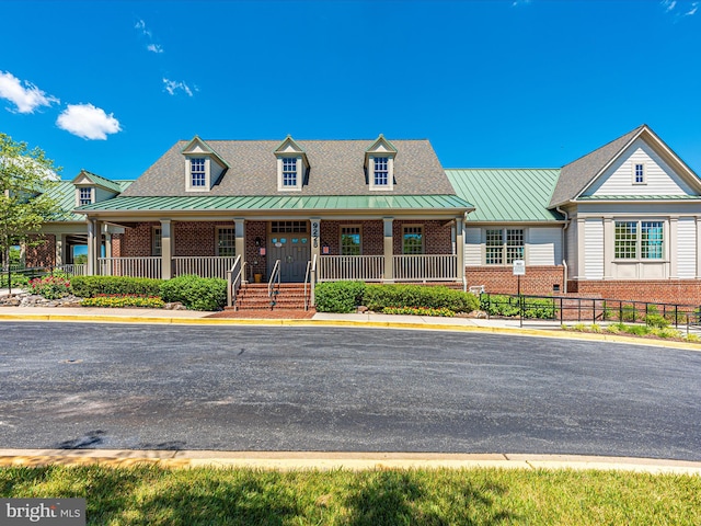 view of front of property with brick siding, a standing seam roof, covered porch, metal roof, and fence