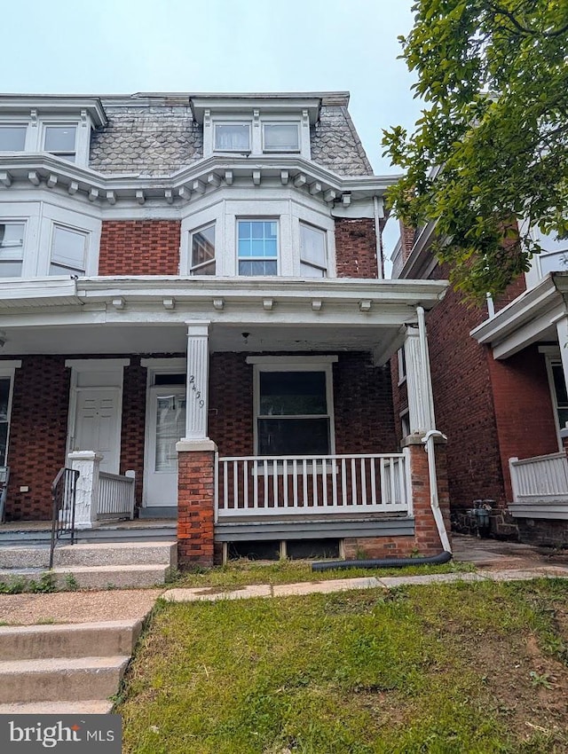 second empire-style home featuring brick siding, mansard roof, and a porch