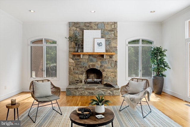 sitting room featuring a stone fireplace, crown molding, wood finished floors, baseboards, and recessed lighting