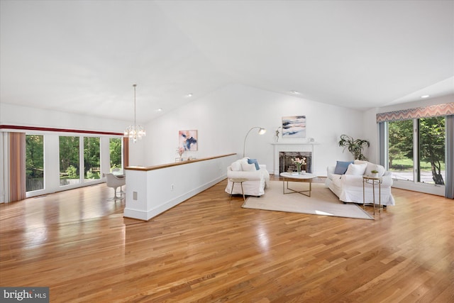 living room featuring vaulted ceiling, light wood-style floors, a chandelier, a high end fireplace, and baseboards