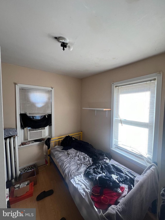 bedroom with radiator, wood finished floors, and cooling unit