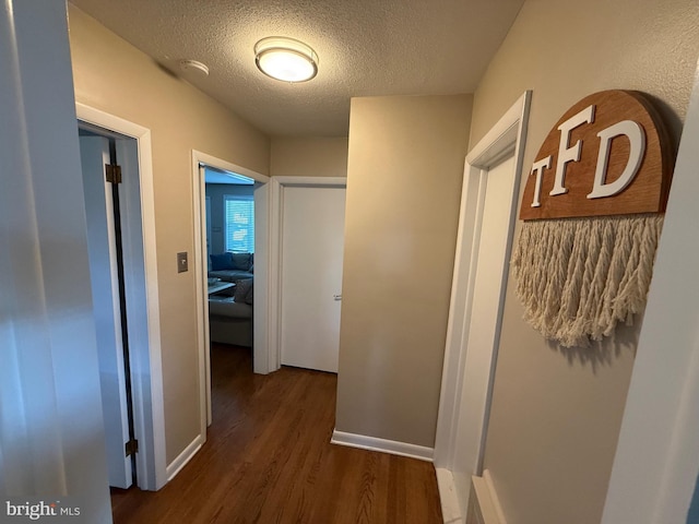 hall with a textured ceiling, baseboards, and dark wood-style floors