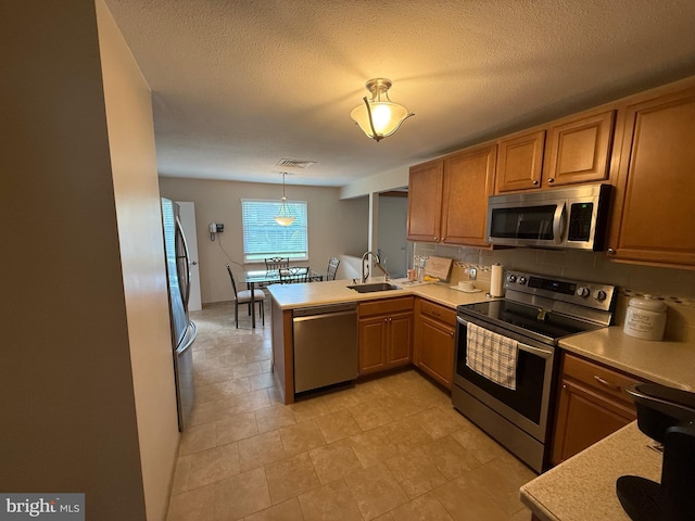 kitchen with a sink, a peninsula, backsplash, light countertops, and appliances with stainless steel finishes