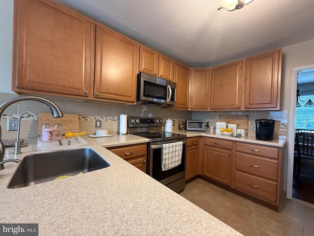 kitchen with a sink, stainless steel appliances, brown cabinetry, light countertops, and tasteful backsplash