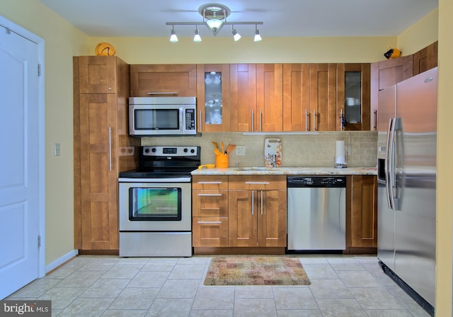 kitchen with appliances with stainless steel finishes, glass insert cabinets, tasteful backsplash, and brown cabinetry