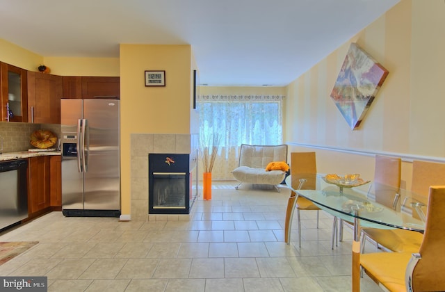 kitchen with glass insert cabinets, brown cabinetry, a tiled fireplace, backsplash, and stainless steel appliances