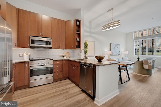 kitchen with a peninsula, a sink, brown cabinetry, light wood-type flooring, and appliances with stainless steel finishes