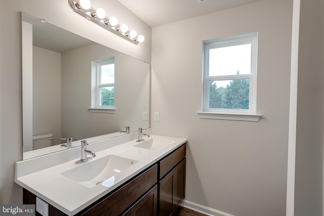 bathroom with toilet, baseboards, double vanity, and a sink