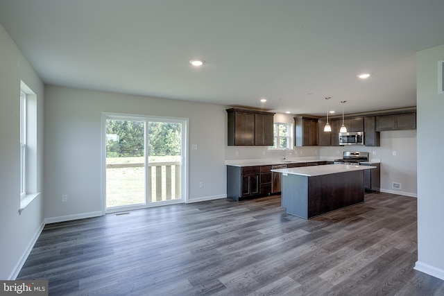 kitchen with a sink, stainless steel appliances, dark brown cabinetry, dark wood-style flooring, and a kitchen island