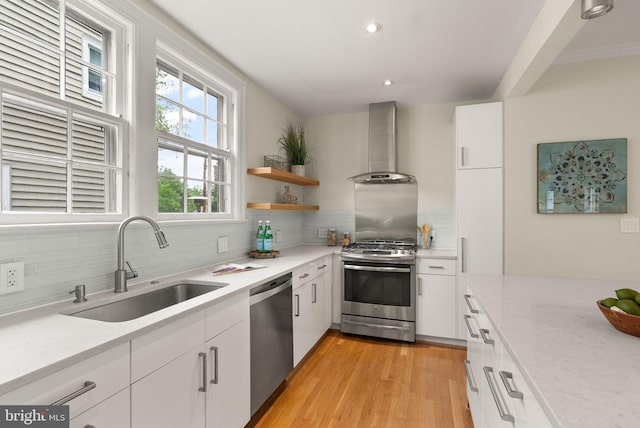 kitchen featuring a sink, stainless steel appliances, white cabinetry, wall chimney range hood, and tasteful backsplash