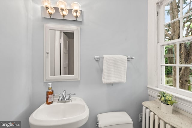 half bath with toilet, radiator, and a sink