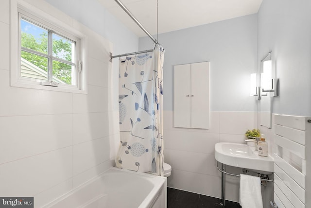 bathroom with tile walls, toilet, shower / bath combination with curtain, and a wainscoted wall