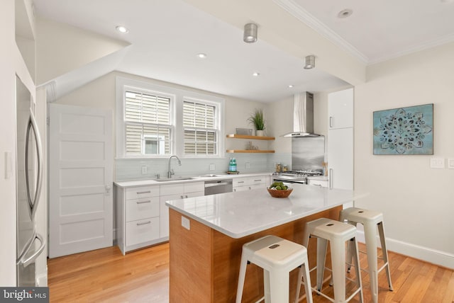kitchen with a kitchen bar, a sink, wall chimney exhaust hood, white cabinetry, and appliances with stainless steel finishes