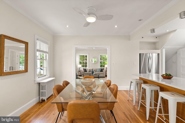 dining space with radiator, light wood-type flooring, baseboards, ceiling fan, and ornamental molding