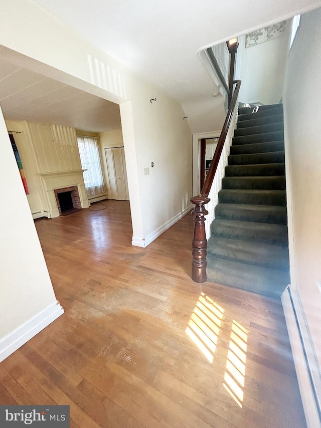stairway featuring baseboards, a baseboard radiator, a fireplace, and wood finished floors